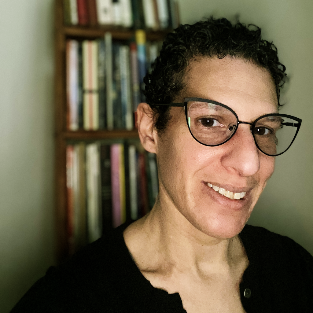 Stacy Kess, a woman with short black curly hair and round cat-eye glasses